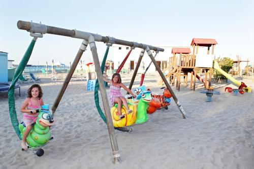 zwei junge Mädchen, die auf Schaukeln auf einem Spielplatz reiten in der Unterkunft Hotel Colorado in Sottomarina