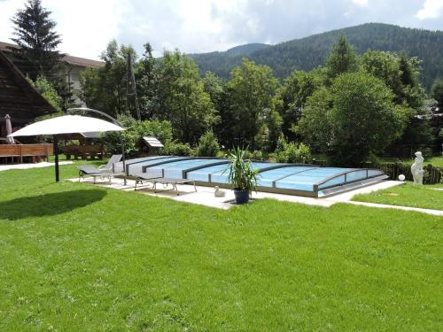 una piscina en un patio con bancos y sombrilla en Haus Kremser, en Bad Kleinkirchheim