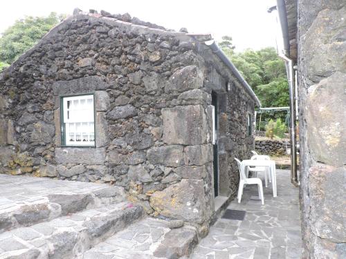 a stone building with a table and a white chair at Casas de Campo HousesInPico in Prainha de Baixo