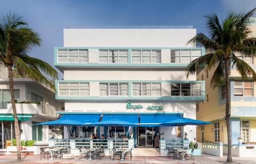 a building with tables and blue umbrellas and palm trees at Penguin Hotel in Miami Beach