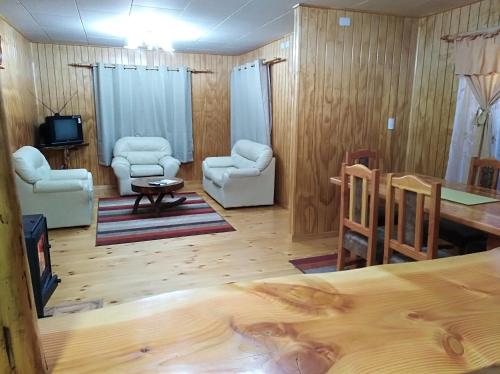 uma sala de estar com pisos e cadeiras de madeira e uma mesa em Cabañas El Maitén em Castro