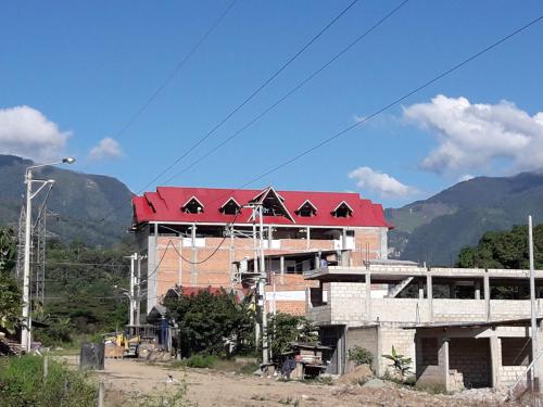 a building with a red roof with mountains in the background at Gran Hotel Virrey in San Ramón