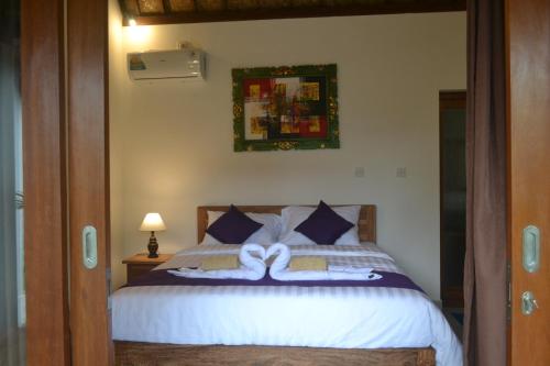 um quarto com uma cama com lençóis brancos e almofadas azuis em Buda Cottage Ubud em Ubud