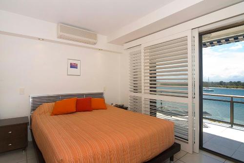 een slaapkamer met een bed met oranje kussens en een balkon bij Commodore Apartments in Noosa Heads