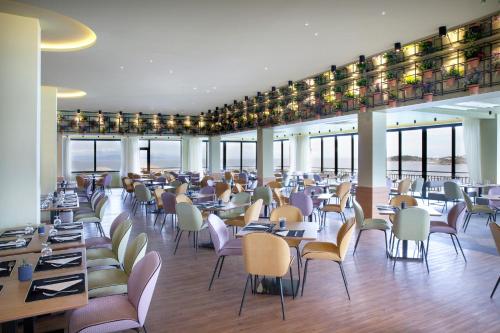 a dining room with tables and chairs and windows at Dolce by Wyndham Athens Attica Riviera in Vravrona