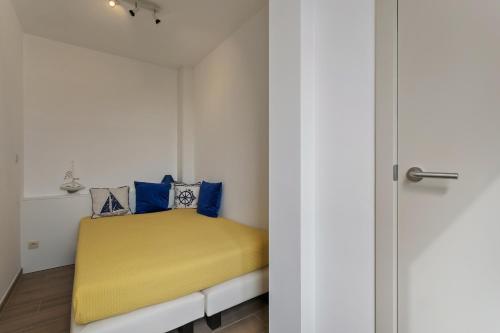 Dormitorio pequeño con cama amarilla y almohadas azules en Apartment V7 en Ostende