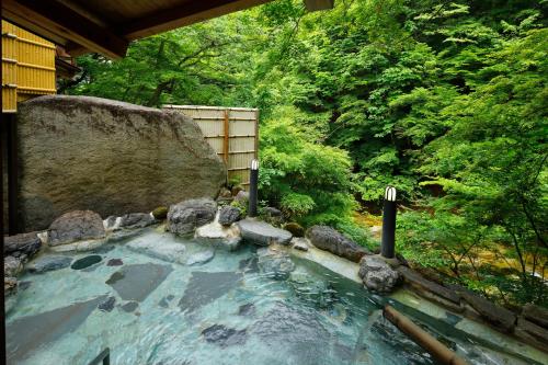 uma banheira de hidromassagem num jardim com pedras e árvores em Hana to Hana em Nikko