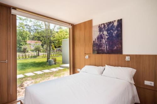 um quarto com uma cama branca e uma grande janela em Bungalow Camping Los Manzanos em Santa Cruz de Oleiros