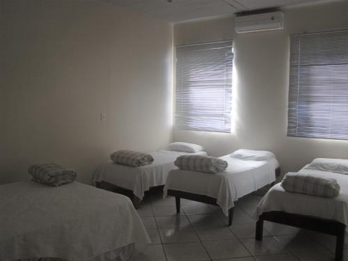 3 camas en una habitación con paredes y ventanas blancas en Pousada Quati, en Foz do Iguaçu