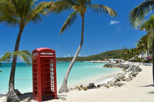 a red phone booth on a beach with palm trees at Antigua Village Beach Resort in Saint Johnʼs