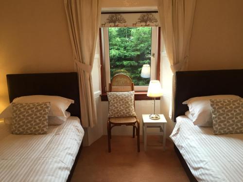 a bedroom with two beds and a window with a chair at Lovat House in Crieff