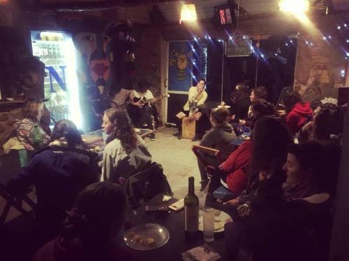 un grupo de personas sentadas en una habitación con un escenario en Giramundo Hostel en Humahuaca