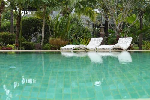two white chairs sitting next to a swimming pool at Mae Nai Gardens in Ban Mae Mae