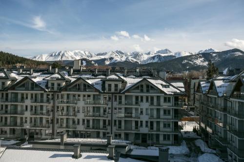 a building with snow covered roofs with mountains in the background at VIP Apartamenty Stara Polana in Zakopane
