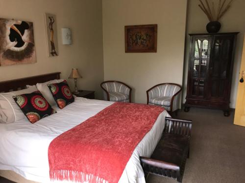 a bedroom with a bed with a red blanket and chairs at Cheetah Lodge Guest House in Hartenbos