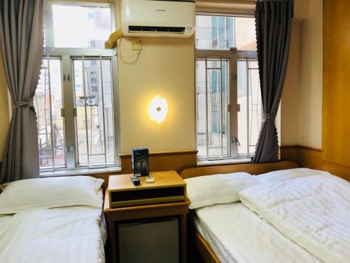 duas camas num quarto com janelas e uma mesa de cabeceira em Good Fortune Inn em Hong Kong