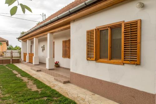 a white house with wooden windows and a yard at Bence Apartman in Tiszabábolna