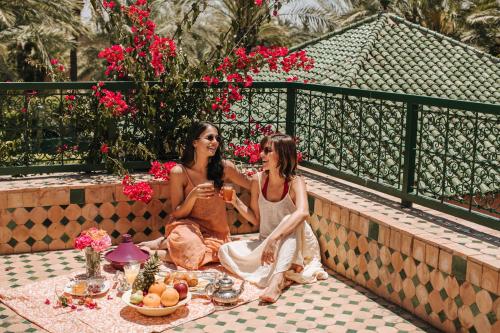 Deux femmes assises sur un mur avec une table de nourriture dans l'établissement Domaine Rosaroum, à Marrakech