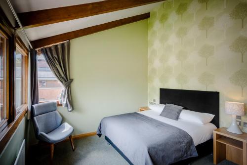 a bedroom with a bed and a chair and a window at Hinxton Hall Hotel and Conference Centre in Hinxton