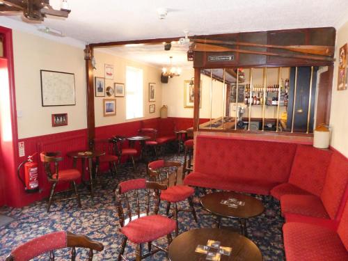 um bar com um sofá vermelho e mesas e cadeiras em The Denewood em Sandown