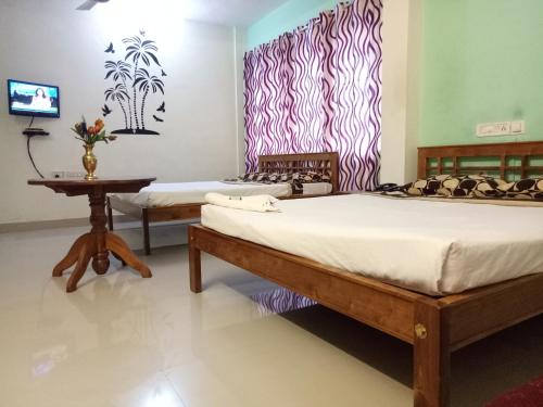 a room with two beds and a table and a tv at Hotel Silver Sand in Trivandrum