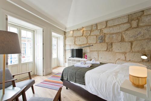 a bedroom with a stone wall with a bed and a tv at RVA - Clerigos Apartments in Porto