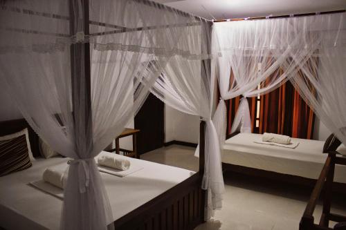 two beds in a room with white curtains at Sigiriya Lahiru Homestay in Sigiriya