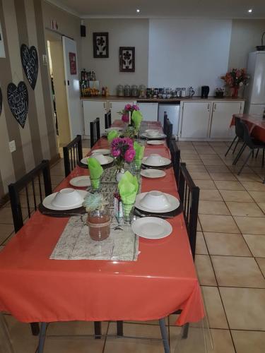 una mesa larga con mantel rojo y flores. en Obrigado Guest House, en De Aar