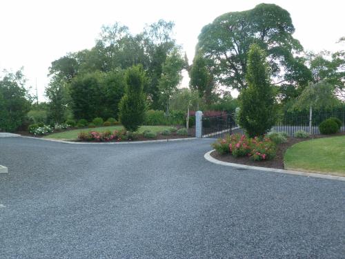 a driveway with a fence and some flowers at Arvalee Retreat With Outdoor HotTub in Omagh
