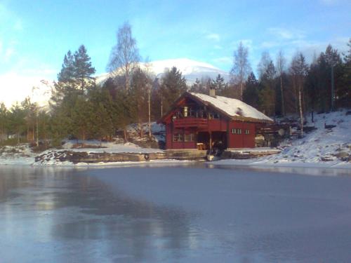 a red cabin with a snow covered roof next to a lake at Naustloftet in Hornindal