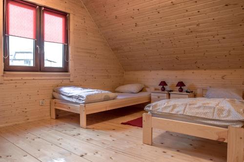 two beds in a wooden room with two windows at Domki Wczasowe Mielenko in Mielenko