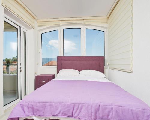a bedroom with a large purple bed with windows at Apartmani Tripović in Tivat