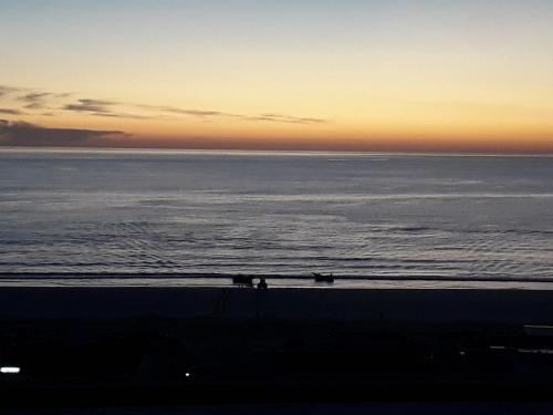 a sunset over the ocean with people walking on the beach at Fonte da Telha Beach Hostel in Costa da Caparica