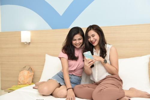 two girls sitting on a bed looking at a cell phone at Hop Inn Hotel Ermita Manila in Manila