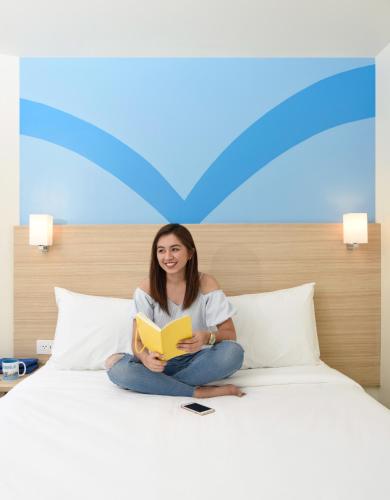 a woman sitting on a bed reading a book at Hop Inn Hotel Ermita Manila in Manila