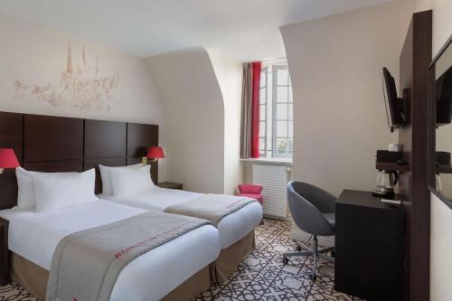 a hotel room with two beds and a television at Best Western Blanche de Castille Dourdan in Dourdan