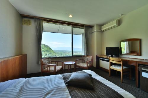 a bedroom with a bed and a desk and a large window at Tateshina Park Hotel in Chino