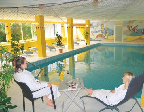 two women sitting in chairs next to a swimming pool at Hotel Heikenberg in Bad Lauterberg