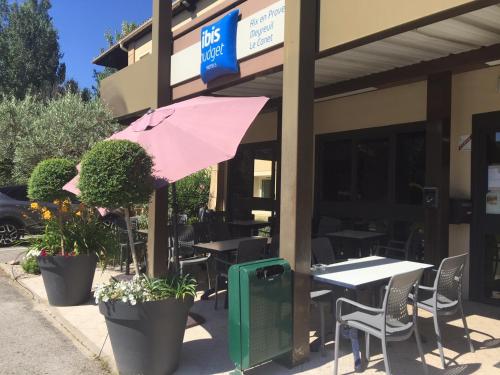 a restaurant with tables and chairs and a pink umbrella at IBIS Budget Aix en Provence Est Le Canet in Meyreuil