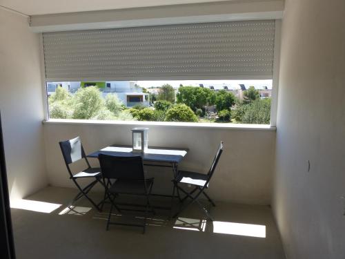une table et des chaises dans une chambre avec une grande fenêtre dans l'établissement Plage des Minimes Résidence Clarines, à La Rochelle
