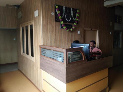 a man is sitting at a desk in a room at Sri Saraswathi Lodge in Tiruchchirāppalli