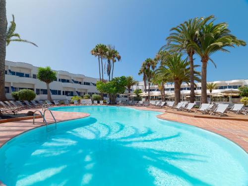 a swimming pool with lounge chairs and palm trees at H10 Ocean Dunas - Adults Only in Corralejo