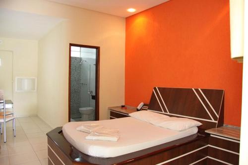 a bedroom with a bed with an orange wall at Motel Passport in Guaratinguetá