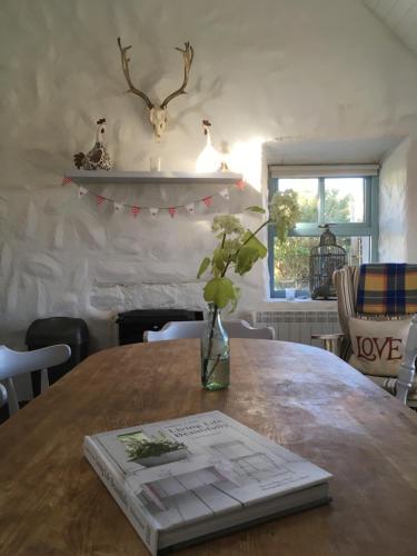 a book on a wooden table with a vase with flowers at The Old Beach Cottage, Achill in Doogort