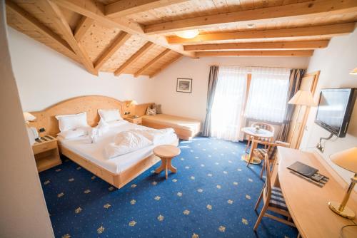 a bedroom with a bed and a desk and a television at Hotel Pra Tlusel in Selva di Val Gardena