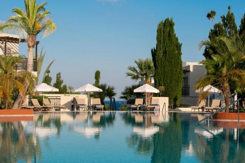 uma piscina com cadeiras e guarda-sóis num resort em Louis Paphos Breeze em Pafos