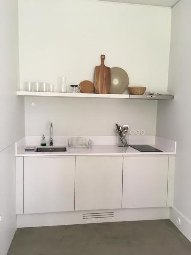 a white kitchen with white cabinets and a sink at Trafaria Garden Beach Houses in Trafaria