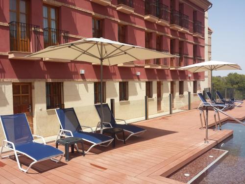 a deck with chairs and an umbrella next to a building at Jardines de La Santa in Totana