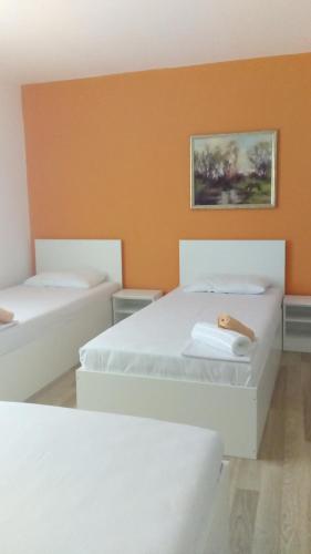 two white beds in a room with an orange wall at Rooms Ela Ela in Prekodolce