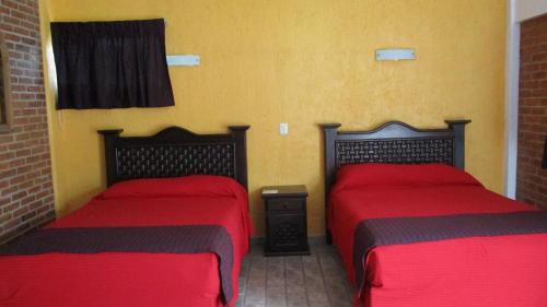 two beds in a room with red sheets at Hotel Villa Monarca Inn in Zitácuaro